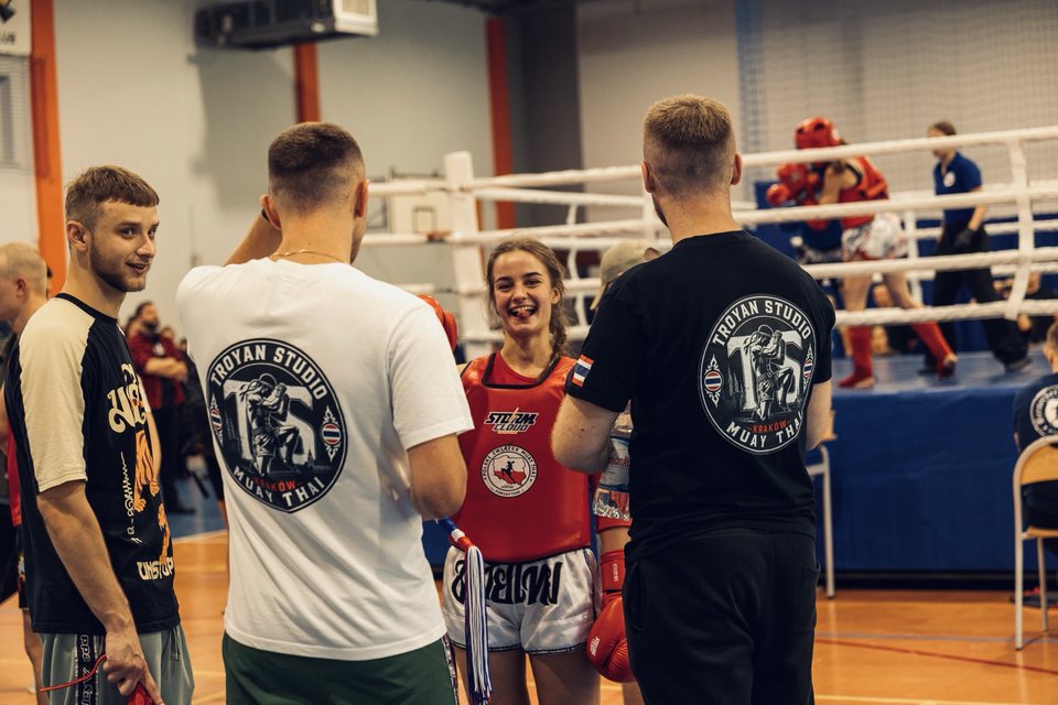 Polina w czerwonym sprzęcie uśmiecha się do trenerów Troyan Studio przed walką